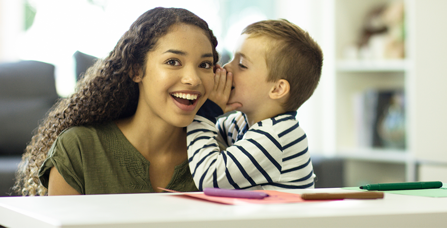 A young boy whispering into his babysitters ear