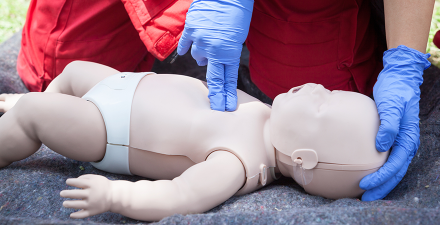 A CPR instructor giving a dummy baby chest compressions