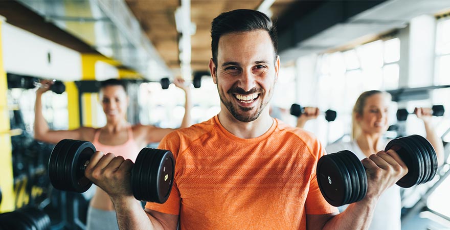 A man smiling at the camera with dumbells in his hand